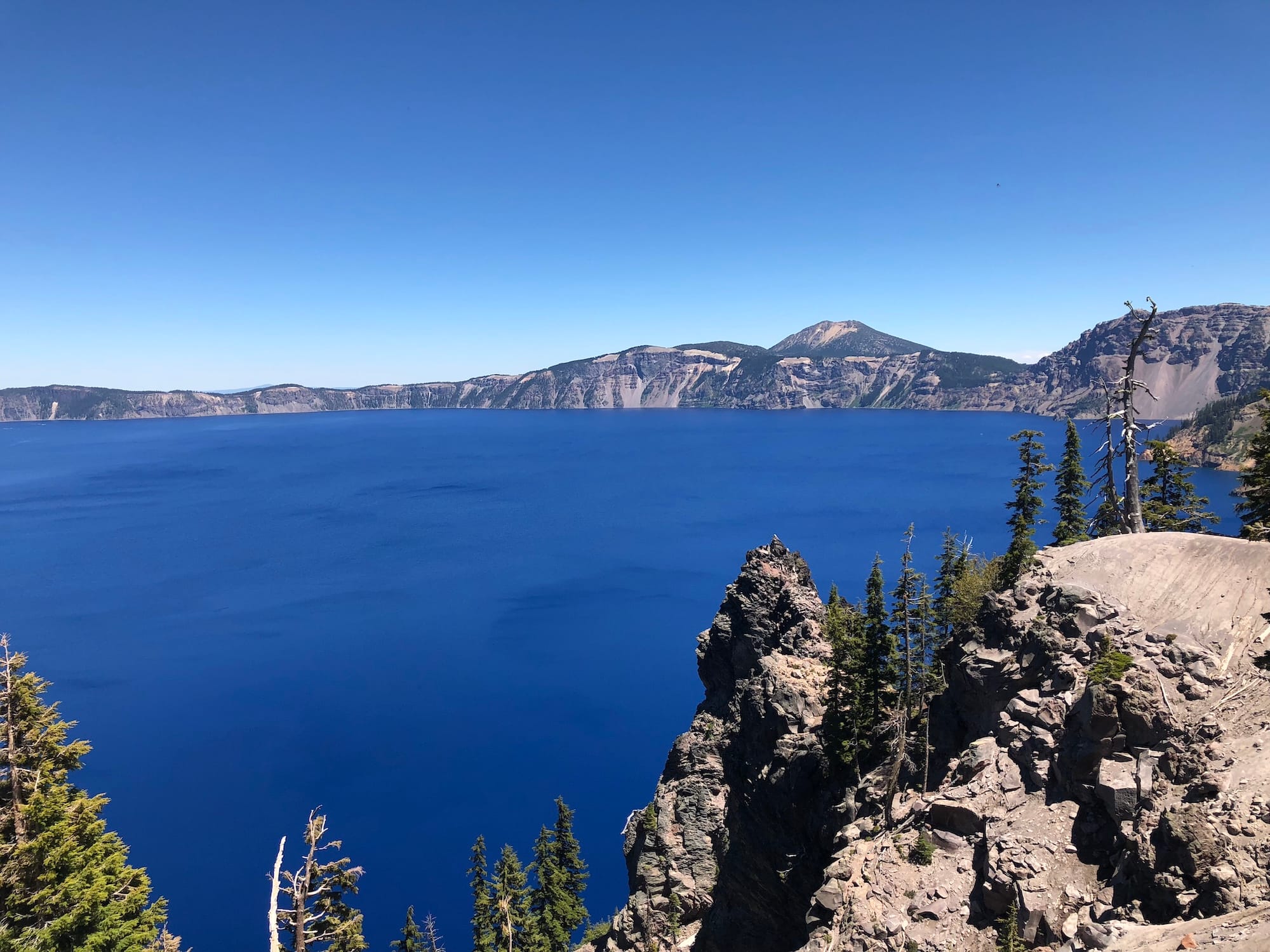 Crater Lake National Park - a deep blue lake with rocky cliffs in the foreground and blue skies above.